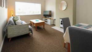 A cozy living room with a sofa, a coffee table, a TV, and a small white cabinet. - Little Lodge (King's Lynn)