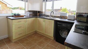 A kitchen with light-colored cabinets, a washing machine, a toaster, and a window with a view of the outside. - Little Lodge (King's Lynn)