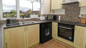 A kitchen with a washing machine, dishwasher, microwave, and a tiled backsplash. - Little Lodge (King's Lynn)