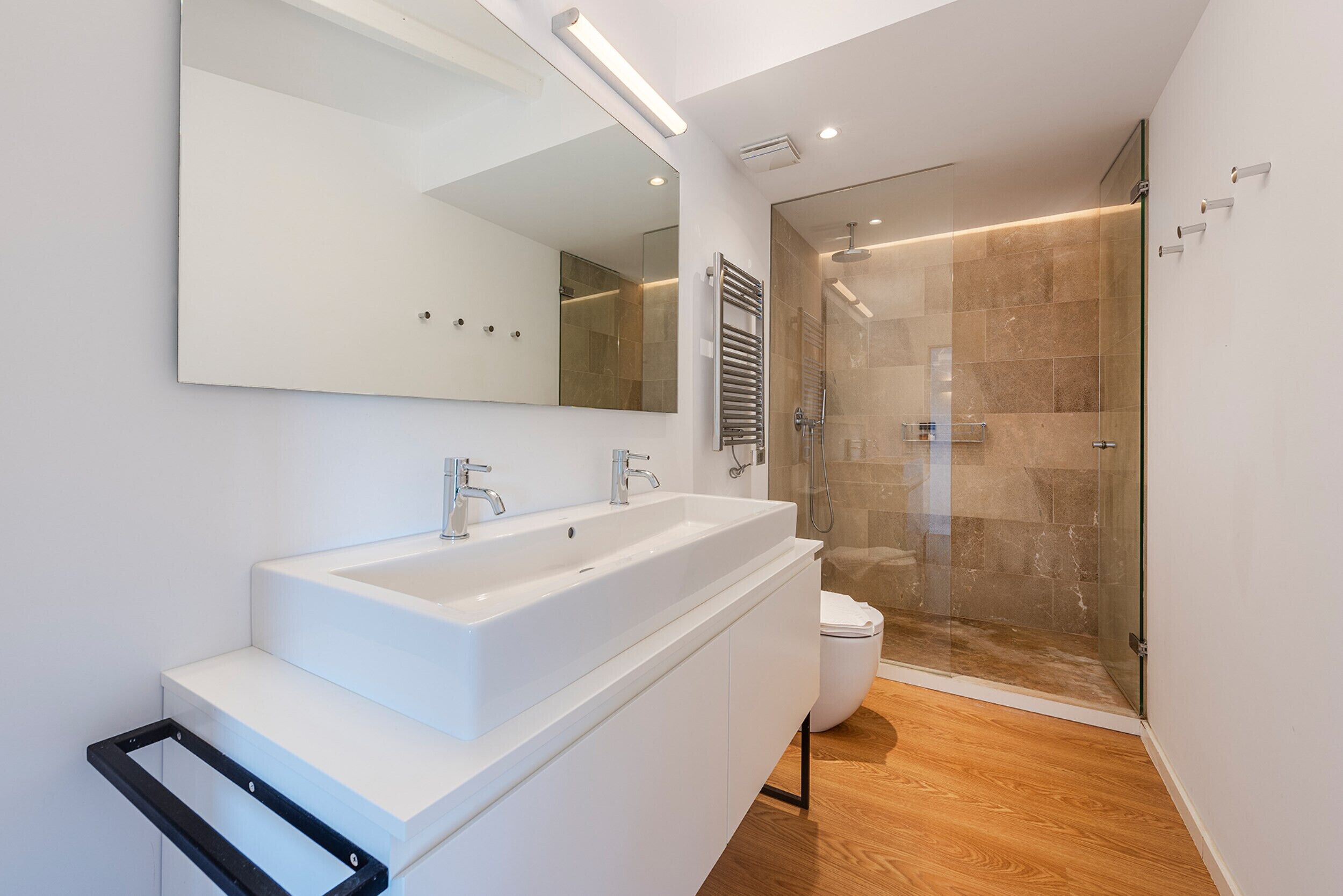 A modern bathroom with a large white sink, a mirror, and a glass-enclosed shower.