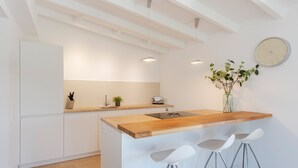 Una cocina moderna con una isla de madera, taburetes blancos tipo bar, un reloj y una planta en maceta.