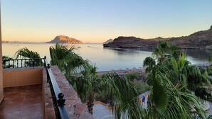 Una terraza con vista a un lago tranquilo, rodeada de palmeras y un paisaje rocoso.