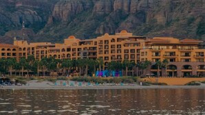 Un hotel con varias construcciones, una masa de agua al frente y montañas como telón de fondo.