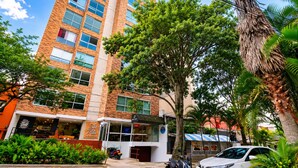 A multi-story building with a brick facade, large windows, and a tree in the foreground. - Stylish Laureles Loft in Medellin (Medellín)