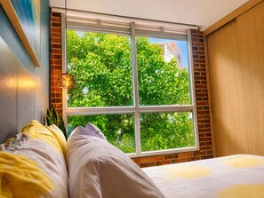 A bedroom with a large window, a bed with white bedding, and a brick wall. - Stylish Laureles Loft in Medellin (Medellín)