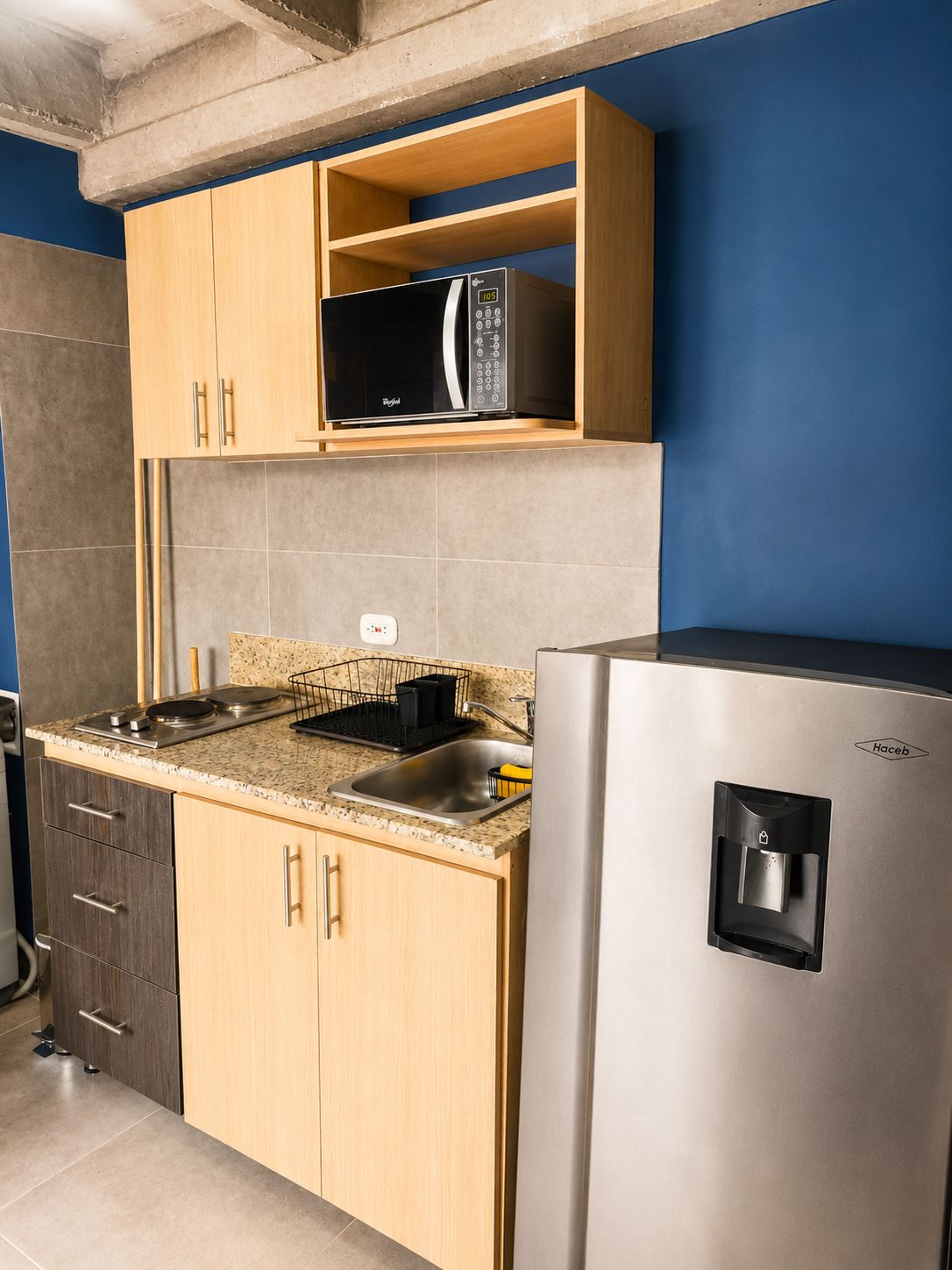 A kitchen with a stainless steel refrigerator, a microwave, and a sink with a dish rack.