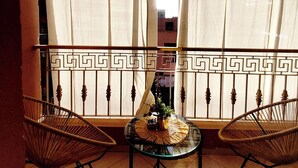 A balcony with two wicker chairs, a glass table with a woven placemat, and a view through sheer curtains.
