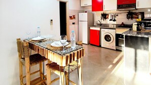 A modern kitchen with red and white cabinets, a built-in washing machine, and a dining area with a glass table and woven chairs.