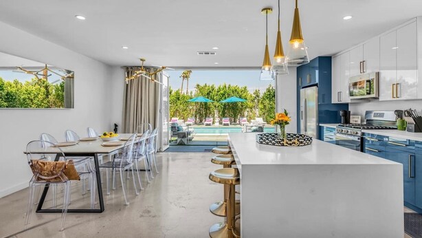 A modern kitchen with a large island, bar stools, and a dining area with clear chairs.