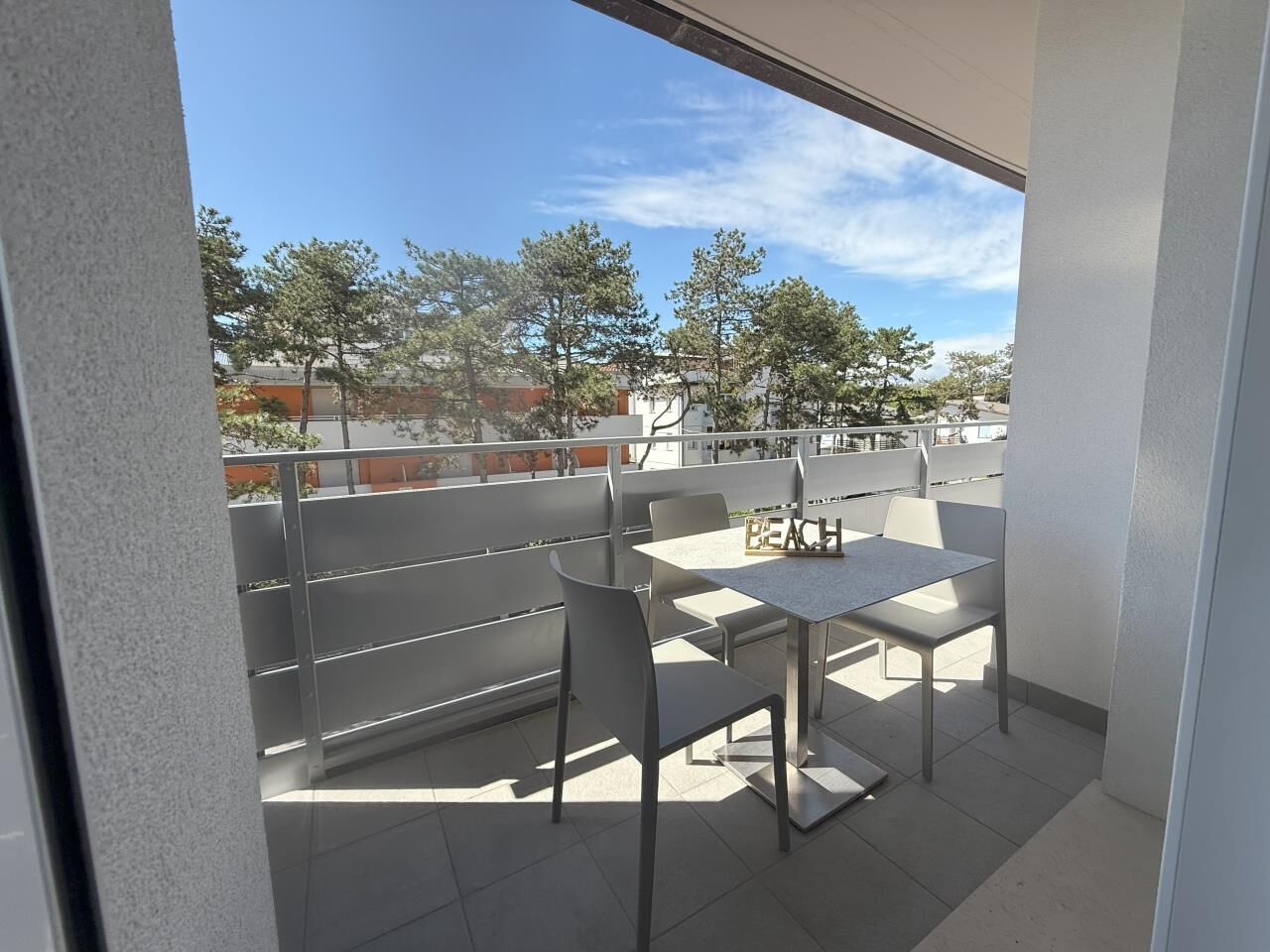 Een balkon met een tafel en stoelen, met uitzicht op een woonwijk met bomen en gebouwen.