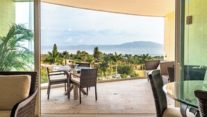 A balcony with wicker furniture, a glass table, and a view of the sea and mountains. - ANANA El Dorado 203 (Ajijic)