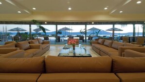 A spacious lounge area with leather sofas arranged around a central coffee table, large windows offering a view of the sea and mountains, and outdoor umbrellas providing shade. - ANANA El Dorado 203 (Ajijic)