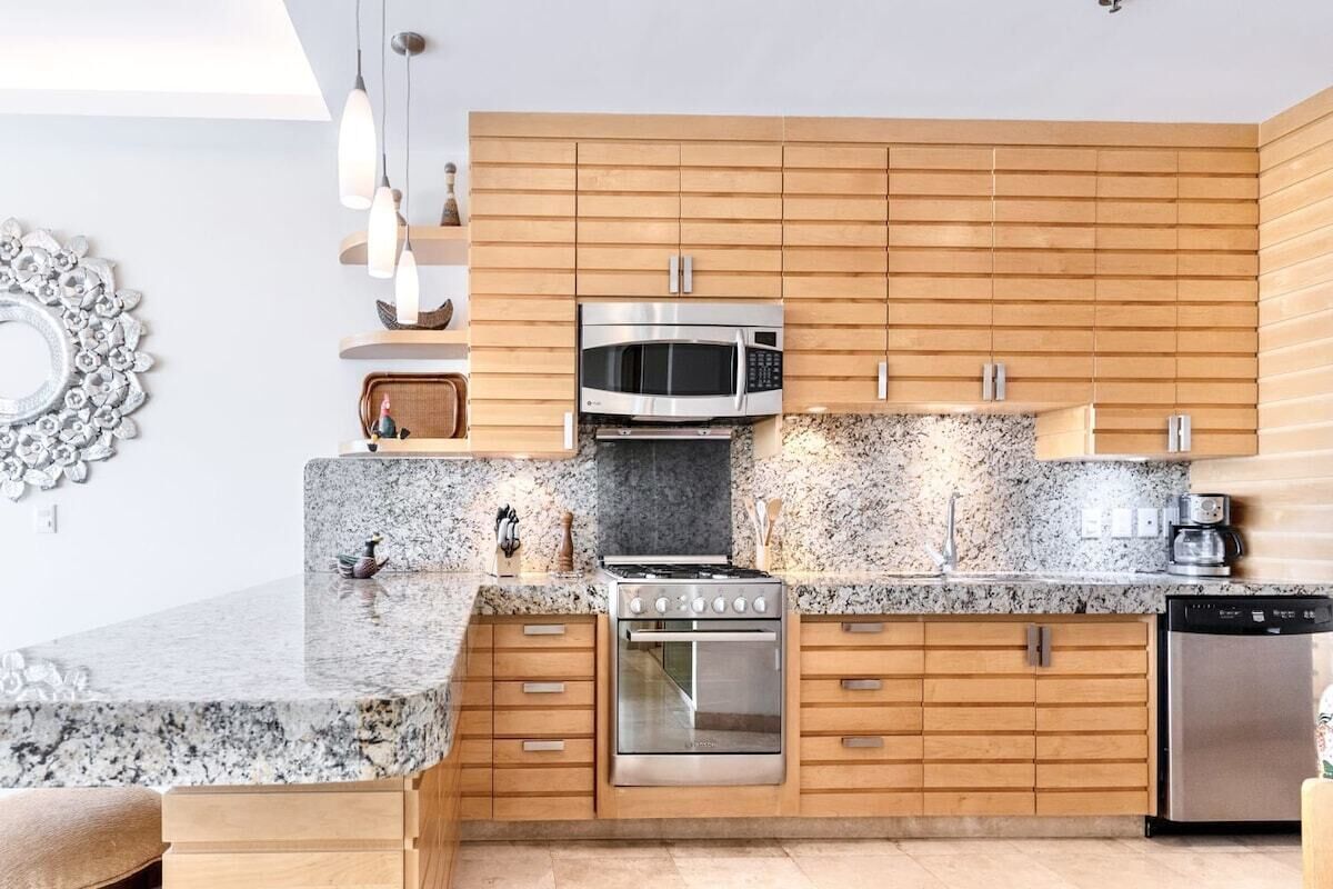 A modern kitchen with wooden cabinets, a granite countertop, a stainless steel microwave, oven, and dishwasher.