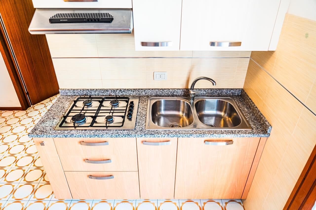 Een kleine keuken met een gasfornuis, een dubbele spoelbak en houten kastjes.
