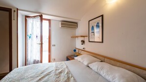 Una camera da letto con un letto, un comodino, un condizionatore d'aria, una finestra con tenda e un quadro appeso al muro.