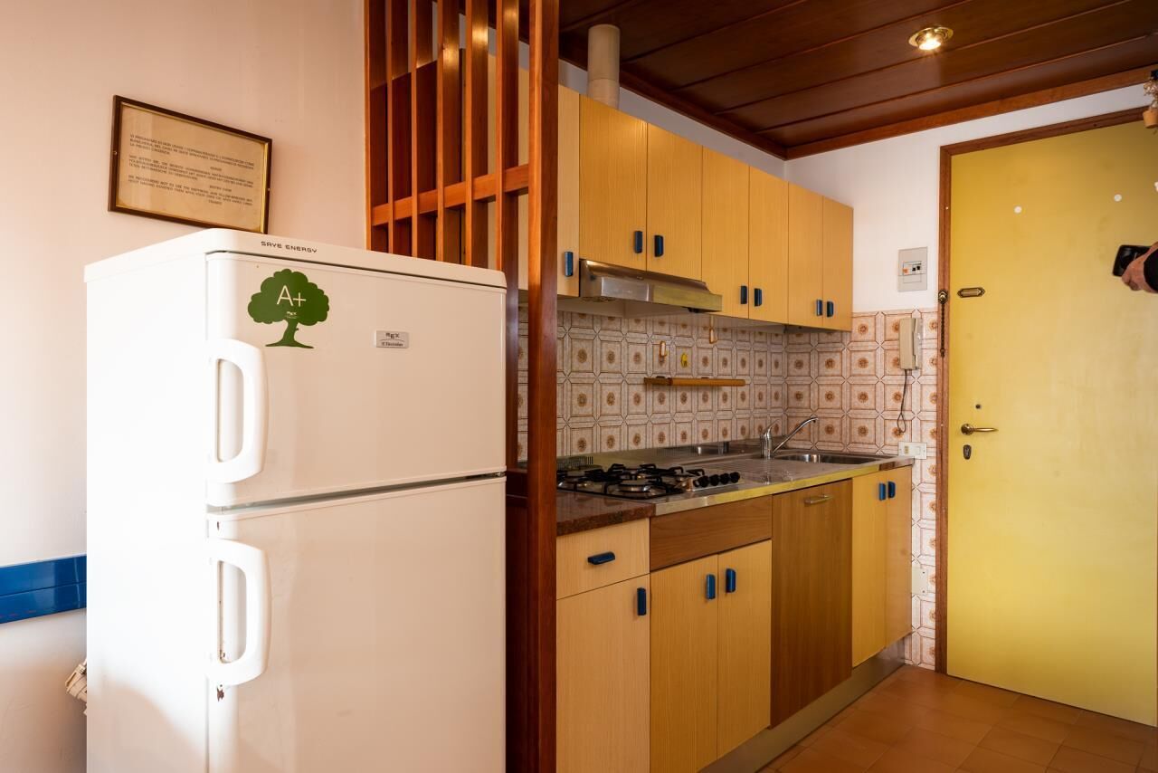 Una cocina compacta con armarios de madera, un refrigerador blanco y un salpicadero de azulejos.