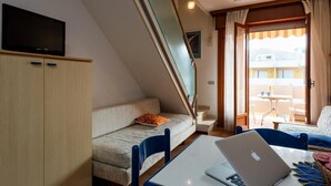 Una camera d'albergo moderna con un divano, un tavolo da pranzo con un portatile, una TV su un mobile e vista sul balcone esterno.