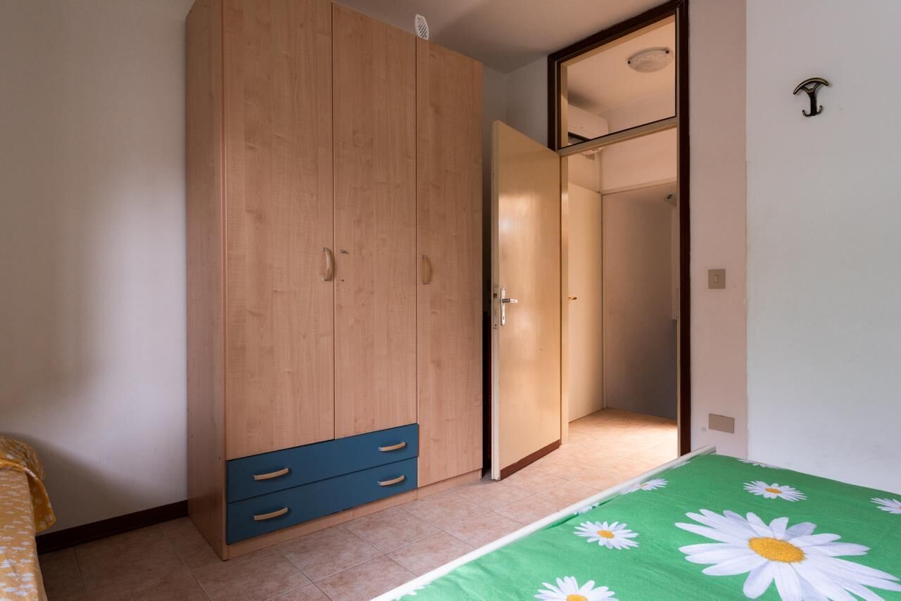 Un dormitorio con un armario de madera, una cama con colcha verde estampada y un espejo sobre el armario.
