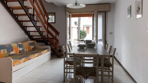 A dining area with a wooden staircase, a sofa with colorful cushions, and a dining table with chairs.