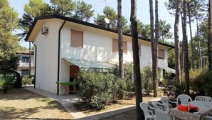 A two-story building with a white exterior, a green awning over the entrance, and a patio area with white plastic chairs and a table.