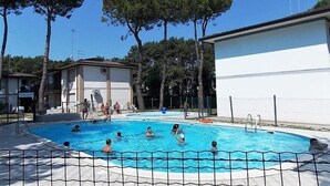 A swimming pool area with a clear blue sky, surrounded by trees and buildings.