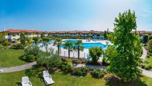 A hotel with a swimming pool surrounded by palm trees and lounge chairs. - Residence Ducale three-room apartment E16 C6*+ for 5 people (Bibione)