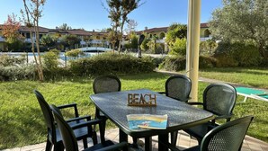 An outdoor patio with a table and chairs, a sign reading "BEACH," and a pool in the background. - Residence Ducale three-room apartment E16 C6*+ for 5 people (Bibione)