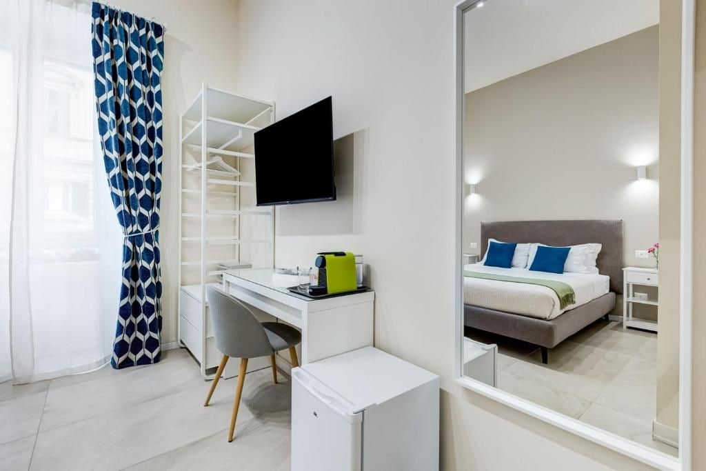 A hotel room with a bed, a desk, a chair, a television, and a wardrobe.