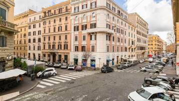 A street view with a row of parked cars, a pedestrian crossing, and buildings with classical architecture.