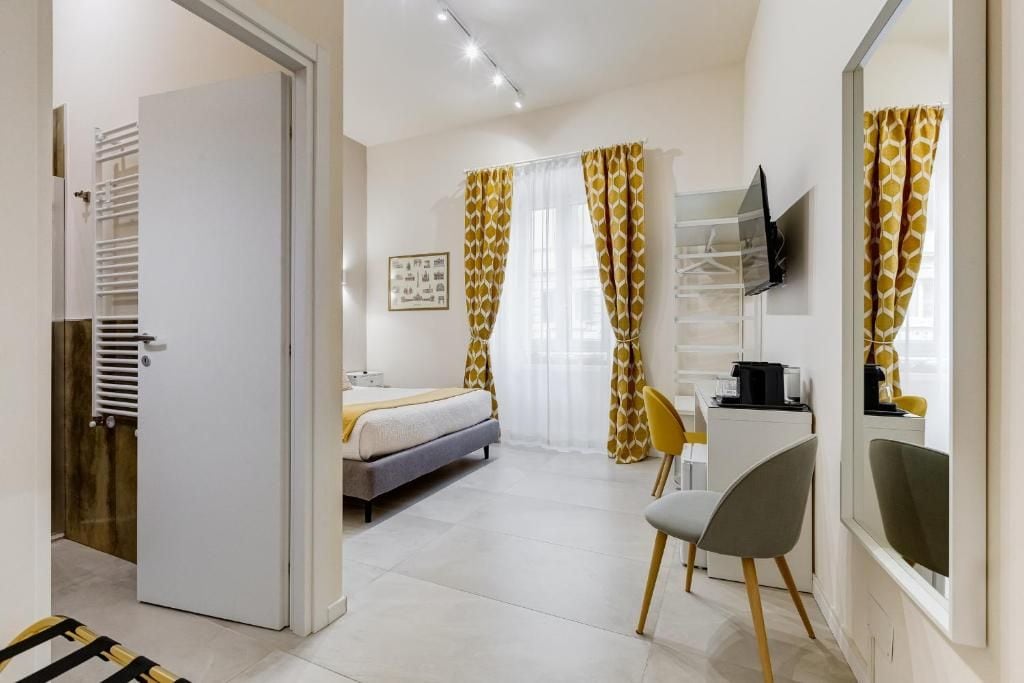Habitación de hotel con una cama, un escritorio con silla, un televisor montado en la pared y un armario.