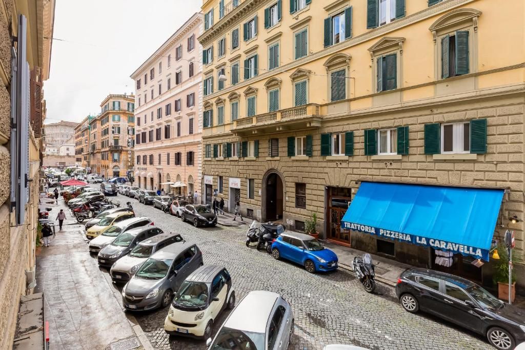 A street view with parked cars, buildings, and a pizzeria with a blue awning.