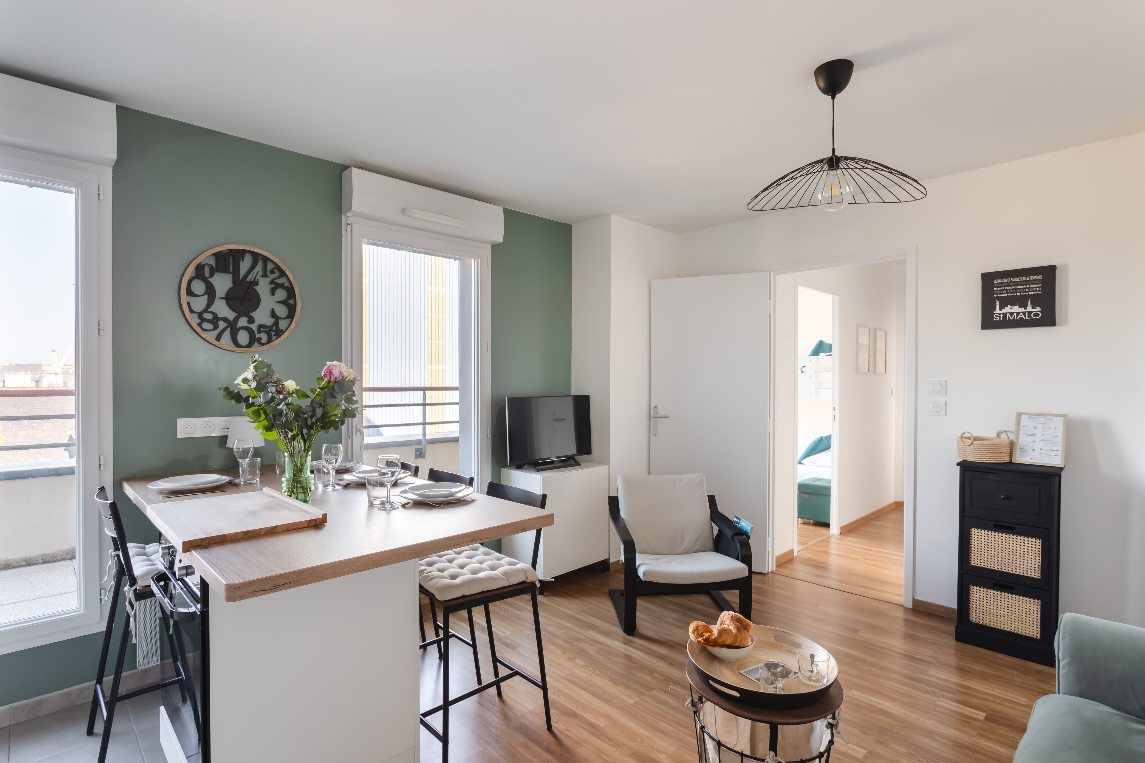 Una cocina moderna con una isla de madera, un área de comedor con sillas, un televisor y un reloj en la pared.