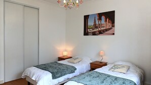 A bedroom with two beds, a chandelier, and a painting on the wall.