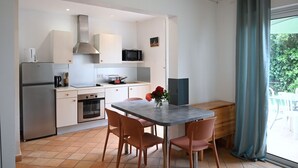 A modern kitchen with white cabinets, a stainless steel refrigerator, a microwave, and a wooden dining table with four chairs.