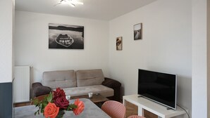 A living room with a sofa, a coffee table, a TV on a stand, and a vase with flowers on a table.