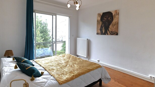 A bedroom with a bed, a window, a radiator, and a painting on the wall.