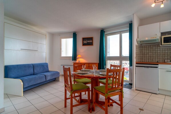 Un espacio habitable compacto con zona de comedor, kitchenette y sofá azul.