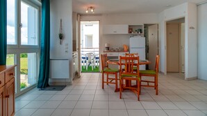 A modern kitchen with white cabinets, a dining area with wooden chairs and a table, and a view of the outdoors through large windows.