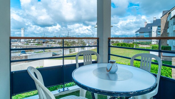 A balcony with a round table and chairs, overlooking a cityscape with buildings and a tower.