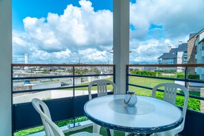 Un balcón con una mesa redonda y sillas, con vista a un paisaje urbano que incluye edificios y una torre.