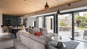 A modern living room with a grey sectional sofa, a round coffee table, and pendant lighting. - Villa Ker Jade - vue sur la mer (Lancieux)