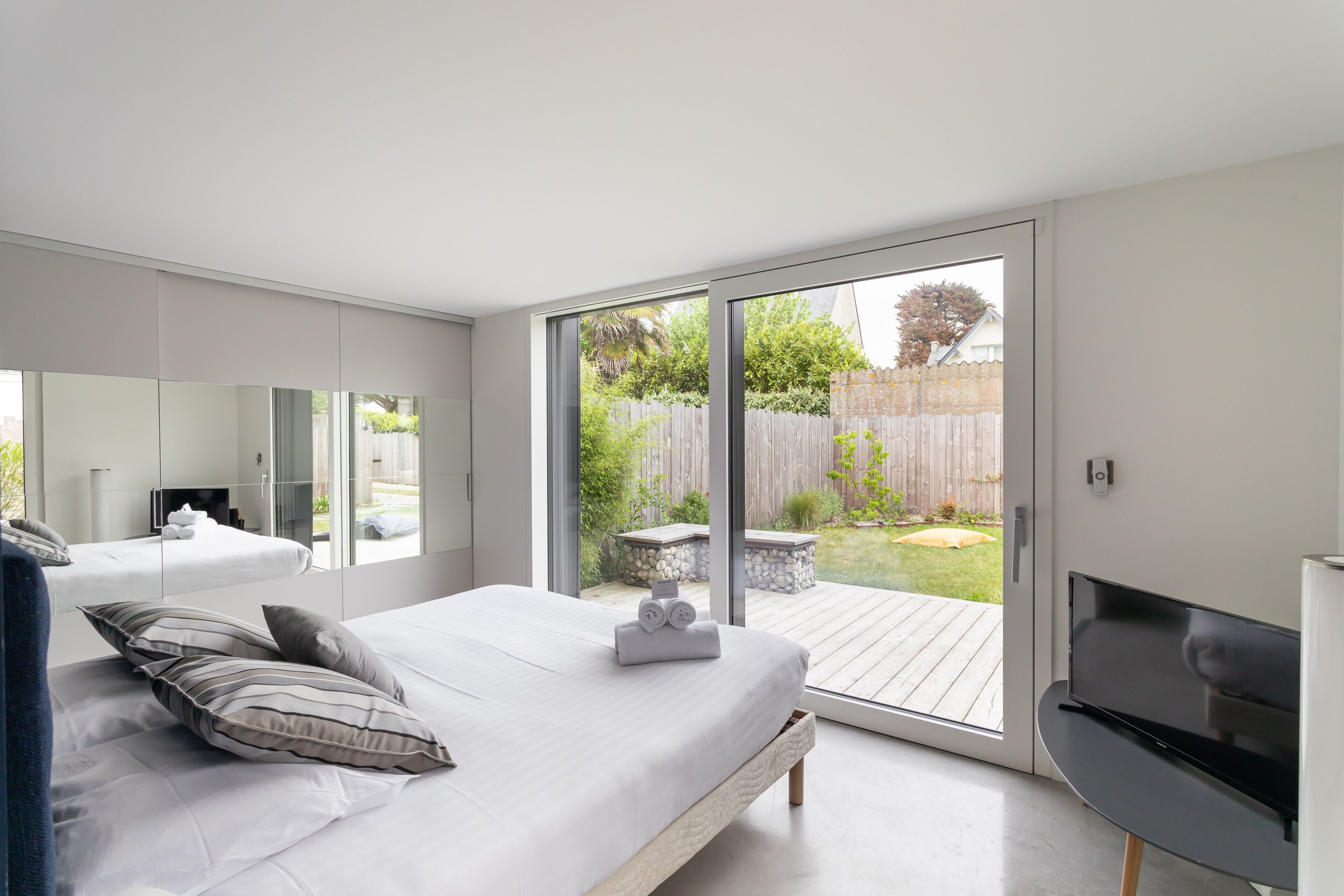 Een moderne slaapkamer met een groot bed, een flatscreen televisie en een schuifdeur die uitkomt op een terras.