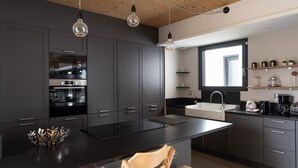 A modern kitchen with dark cabinetry, a central island, and pendant lighting. - Villa Ker Jade - vue sur la mer (Lancieux)