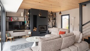 A modern living room with a sofa, a TV, bookshelves, and a fireplace. - Villa Ker Jade - vue sur la mer (Lancieux)