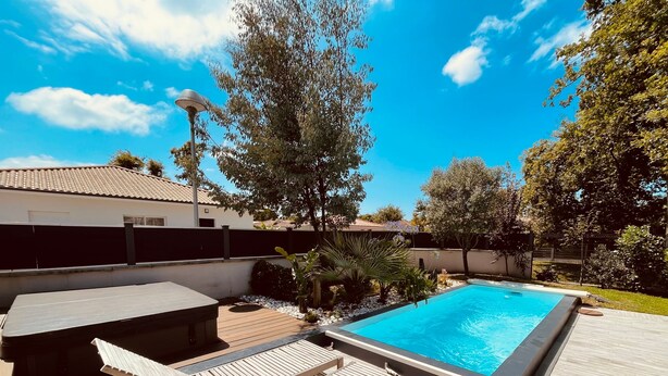Una piscina rectangular con terraza de madera, sillas de descanso y un jacuzzi.