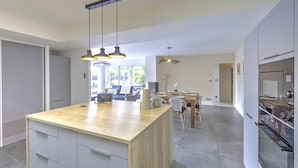 Una cocina moderna con isla de madera, iluminación colgante y comedor con sillas y mesa.