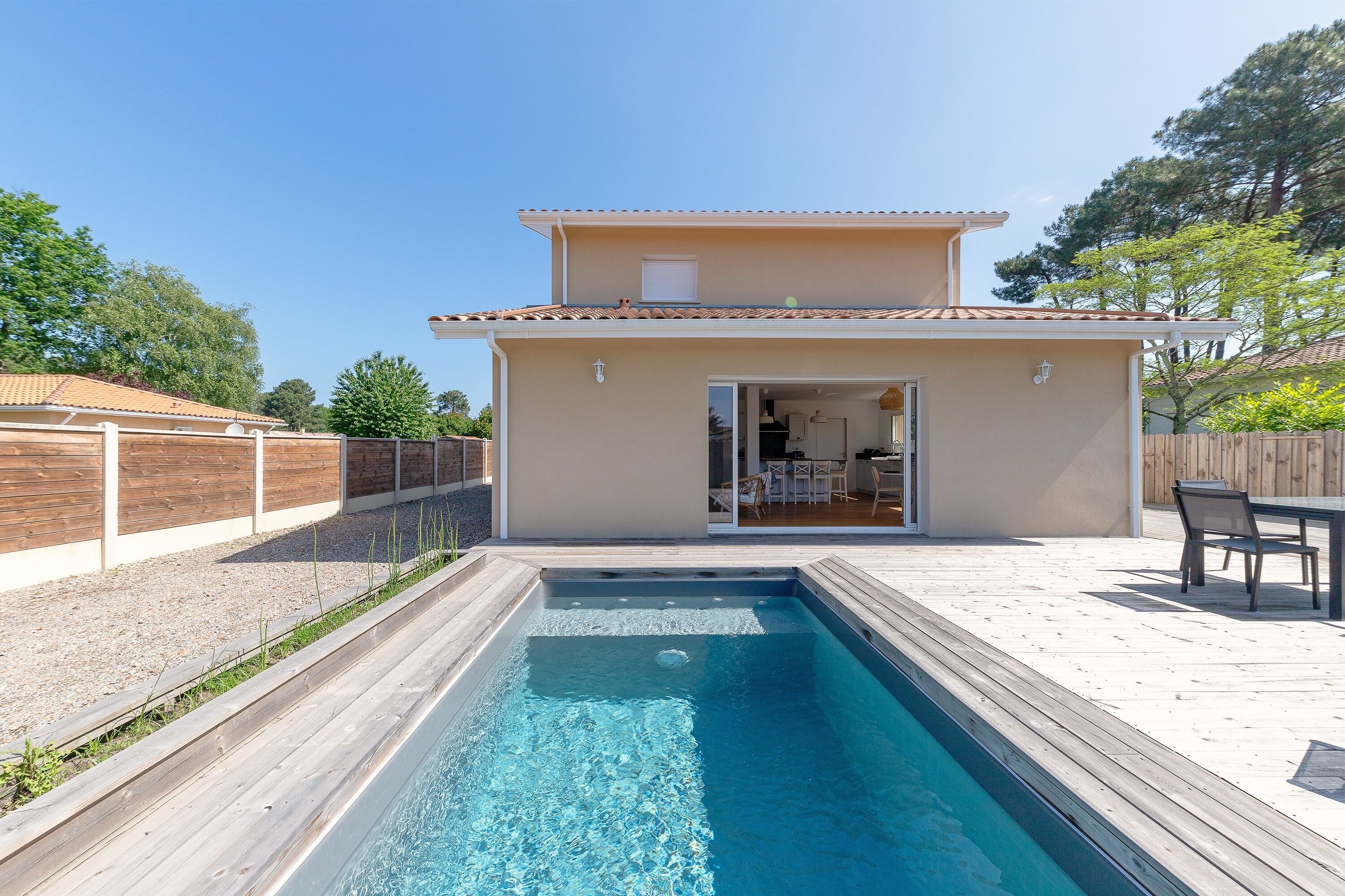 Une piscine avec une terrasse en bois, un patio couvert et un bâtiment doté d’une porte-fenêtre coulissante.