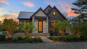 A modern house with a stone facade, a prominent front door, and a landscaped front yard. - Newly built luxury home with pool, hot tub, McKinley Beach access (Union Pier)