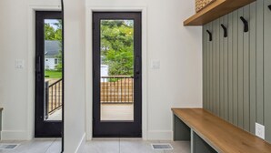 Un pasillo con dos puertas negras que dan a un balcón, un banco de madera y un estante con ganchos.