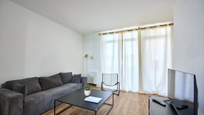 A modern living room with a grey sofa, a black coffee table with a plant, a black chair, and a TV on a stand.